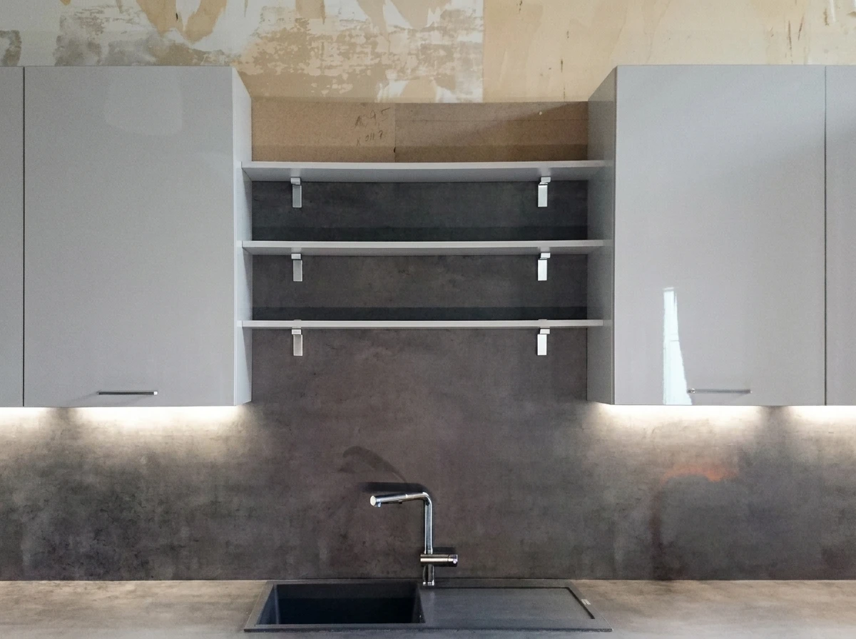 Cuisine moderne minimaliste avec îlot central en bois clair, plan de travail blanc, étagères murales ouvertes noires, réfrigérateur gris anthracite intégré