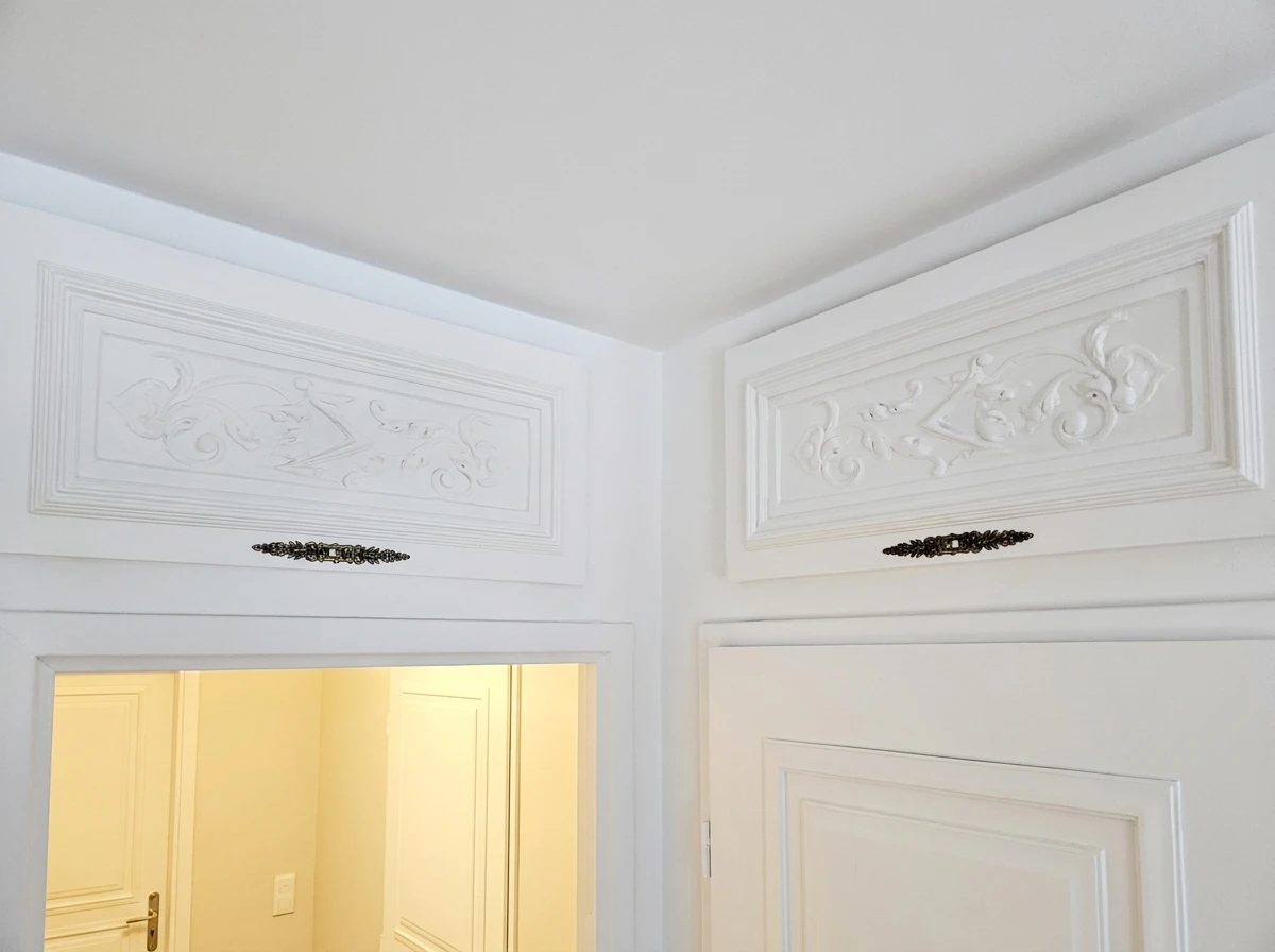 Salon lumineux avec plafond blanc orné de deux rosaces en plâtre à motif concentrique en relief