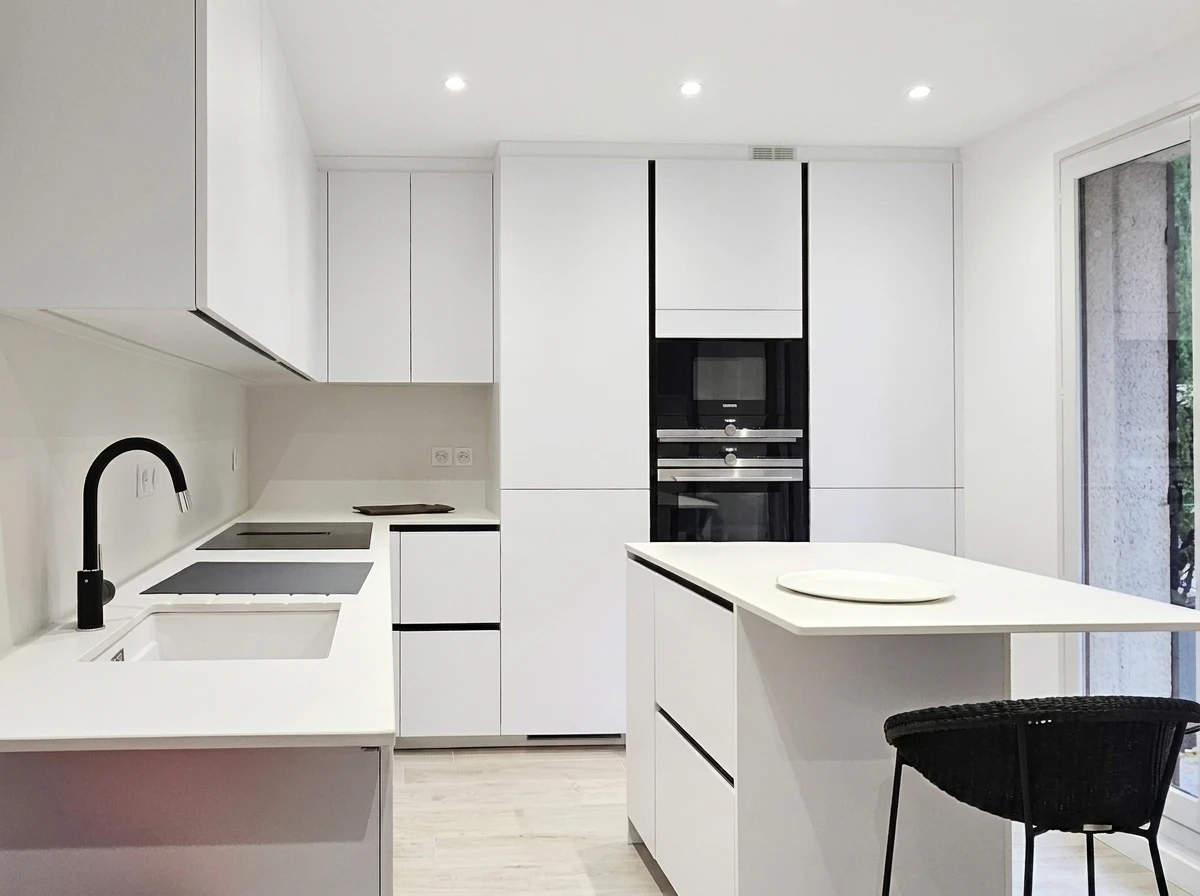 Cuisine moderne ouverte avec îlot central équipé de plaques à induction, escalier flottant en bois et métal à l'arrière-plan