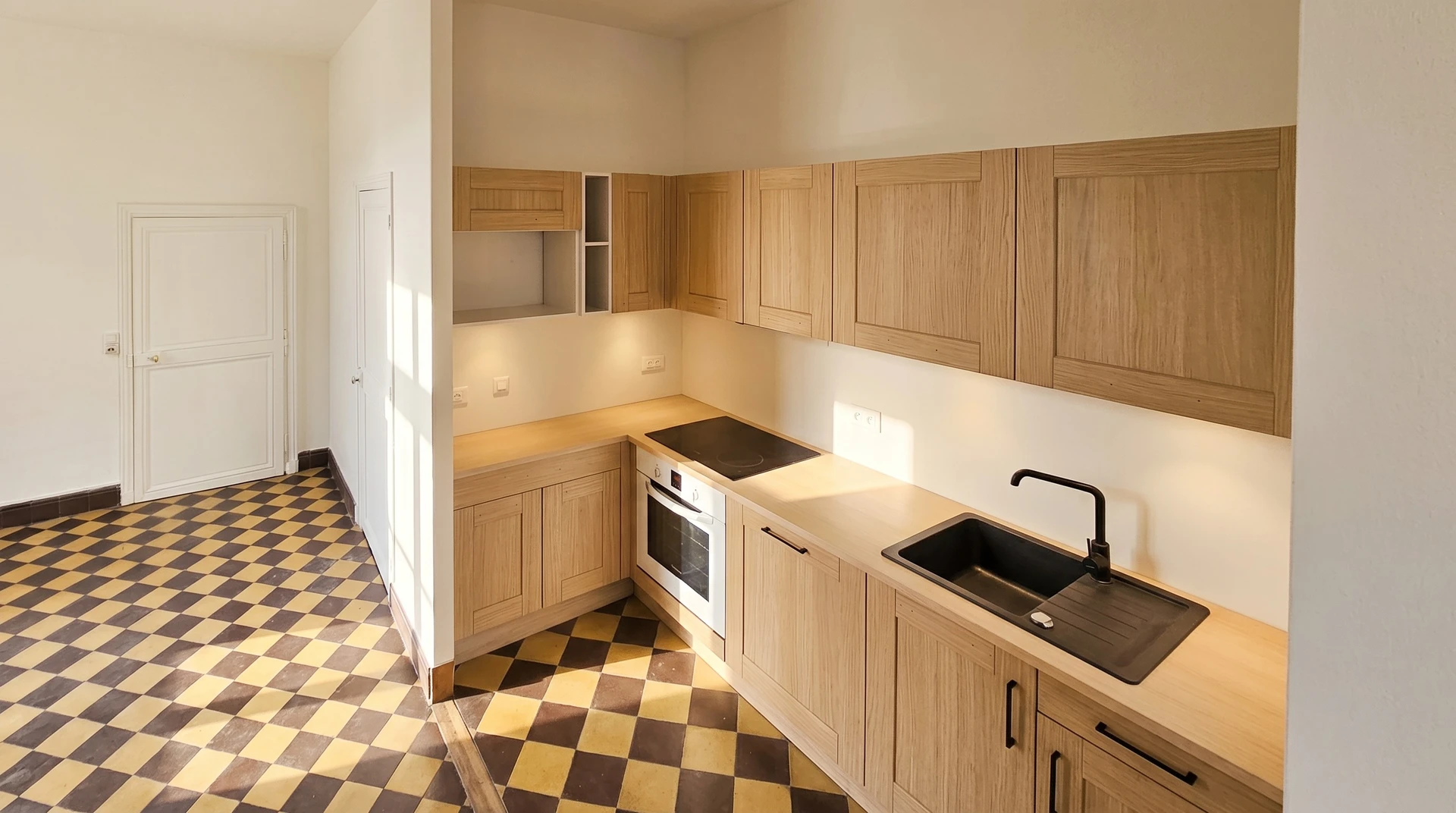 Cuisine moderne épurée avec plan de travail en pierre naturelle beige, évier intégré et robinetterie noire arquée